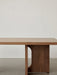 A close-up of the Androgyne Lounge Table in walnut, highlighting the smooth wooden tabletop and the arched leg design.