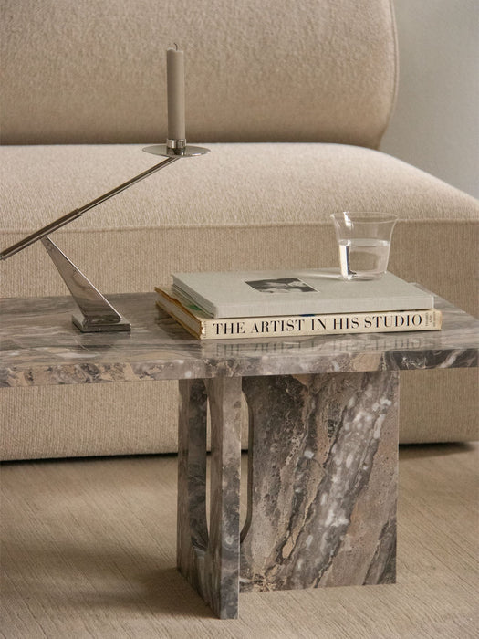 A close-up of the Androgyne Lounge Table in Grey Galaxy marble, styled with books and a candle holder next to a cream sofa.