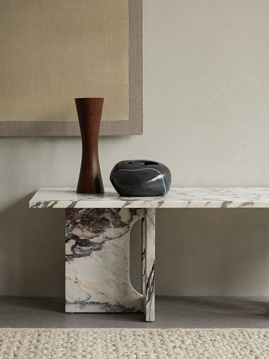 The Androgyne Lounge Table in Calacatta Viola marble, styled with a tall wooden vase and a low, round black ceramic object.