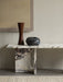 The Androgyne Lounge Table in Calacatta Viola marble, styled with a tall wooden vase and a low, round black ceramic object.