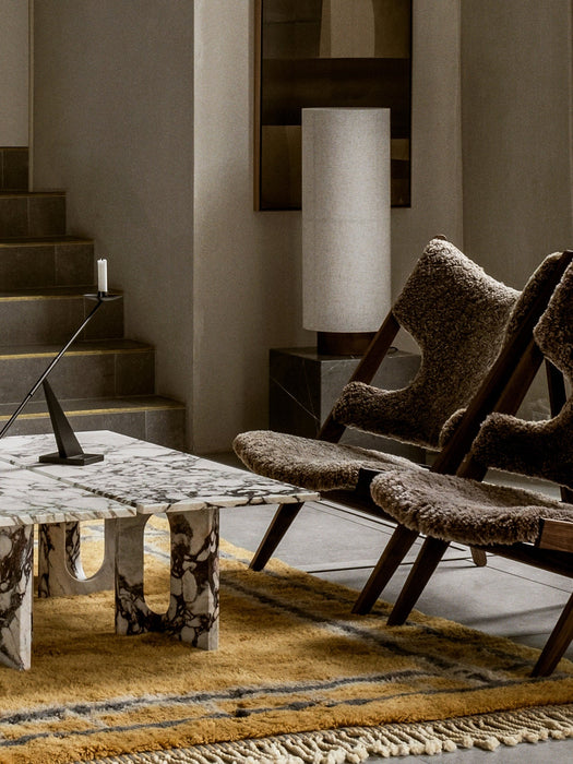 The Androgyne Lounge Table in Calacatta Viola marble, set on a yellow and grey rug next to two brown shearling chairs.