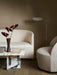 The Androgyne Lounge Table next to a Tearoom Sofa, Lounge Chair, and Wing Floor Lamp in a softly lit living room setting.