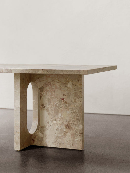 A close-up of the Androgyne Lounge Table in Kunis Breccia stone, focusing on its thick, sculptural leg with an oval cutout.