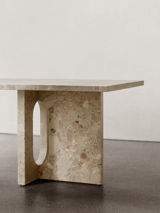 A close-up of the Androgyne Lounge Table in Kunis Breccia stone, focusing on its thick, sculptural leg with an oval cutout.