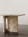 A close-up of the Androgyne Lounge Table in Kunis Breccia stone, focusing on its thick, sculptural leg with an oval cutout.
