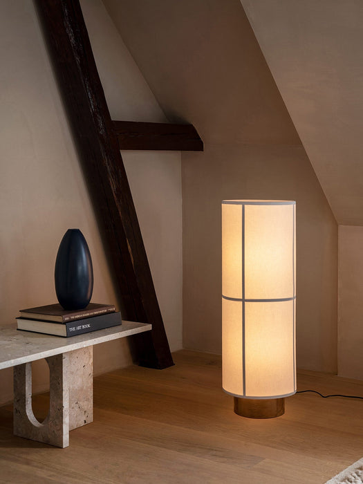 The stone Androgyne Lounge Table with books and a vase, next to an illuminated floor lamp in a room with wooden beams.