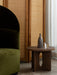A dark oak Androgyne Side Table with a Strandgade Stem Vase and glass, next to a green velvet Tearoom Lounge Chair.