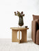 A natural oak Androgyne Side Table styled with a vase of flowers and a small bowl, set beside a brown sofa on a ribbed rug.