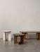 Three Androgyne tables on a grey floor: a white base/marble top side table, a dark oak side table, and a light oak bench.