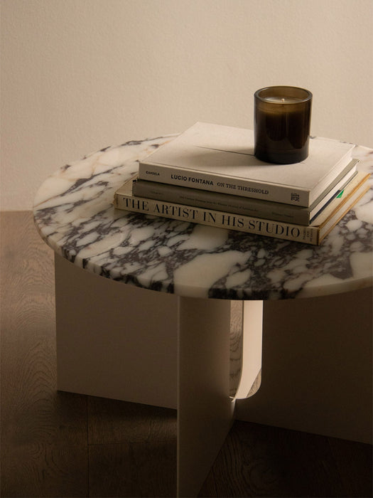 Close-up of the Androgyne Side Table with a white and grey marble top and an ivory base, styled with books and a candle.