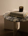 Close-up of the Androgyne Side Table with a white and grey marble top and an ivory base, styled with books and a candle.