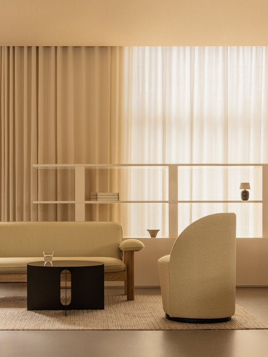 A warm-toned living room featuring a beige Brasilia Sofa, a black Androgyne Side Table, and a curved Tearoom Side Chair.