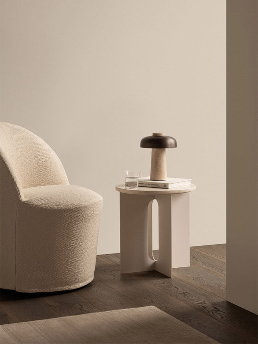 A cream Tearoom Club Chair Swivel beside an Androgyne Side Table with a book, glass and Reverse Table Lamp Portable.