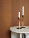Close-up of two Duca Candlesticks holding white candles on an Androgyne Side Table with a marble top against a dark wood wall