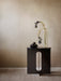 The black Androgyne Side Table with a marble top, featuring a central cutout, styled with vase and bowl against a beige wall.