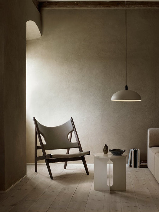 A tranquil room setting featuring the wooden Knitting Chair next to an Androgyne Side Table, lit by a Hubert Pendant lamp.