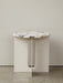 Androgyne Side Table with an ivory base and a veined marble top, standing on a terrazzo floor against a light grey wall.