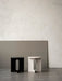 The Androgyne Side Table shown in black with a dark marble top and in ivory, standing side-by-side in a minimalist room.