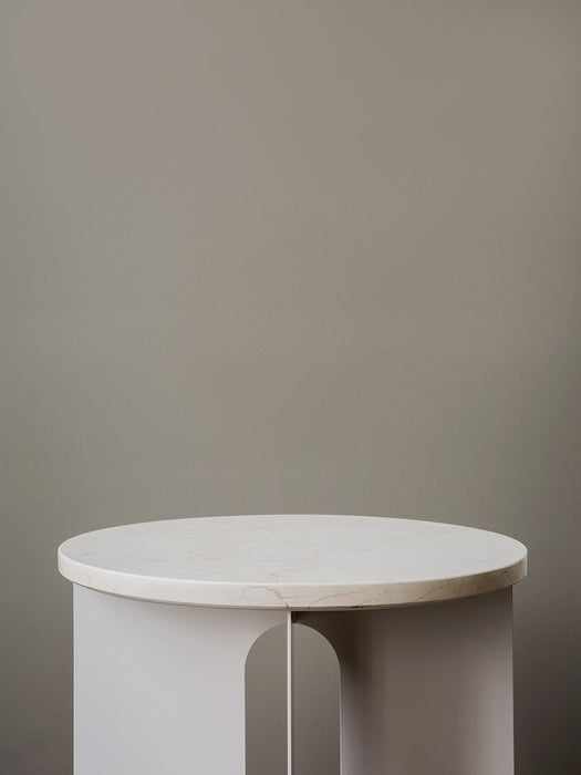A detailed close-up of the Androgyne Side Table, showing its round white marble top on an ivory powder-coated steel base.