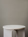 A detailed close-up of the Androgyne Side Table, showing its round white marble top on an ivory powder-coated steel base.
