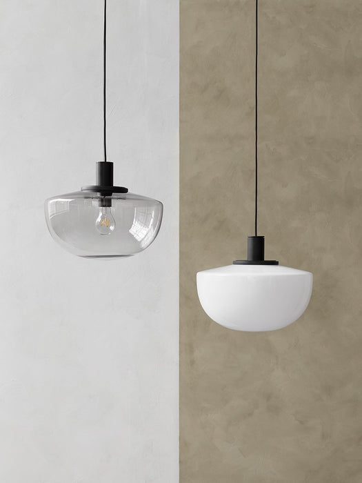 Two Bank Pendant lights, one with a smoked glass shade and one with an opal glass shade, hang against a split-tone wall.