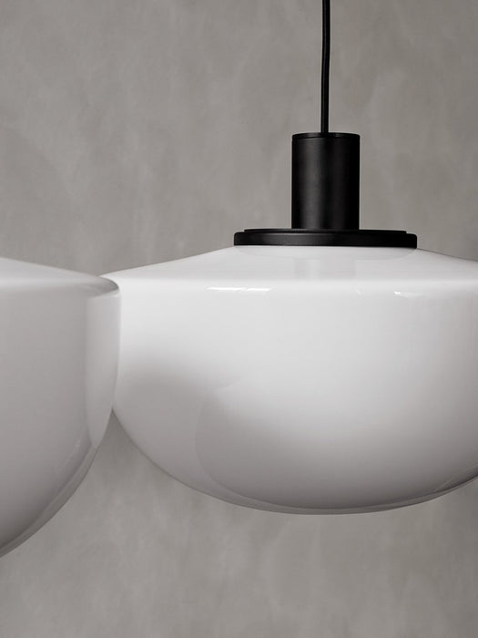 A close-up of the Audo Bank Pendant, showing the white opal glass shade and black aluminium fitting against a grey wall.