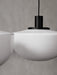A close-up of the Audo Bank Pendant, showing the white opal glass shade and black aluminium fitting against a grey wall.
