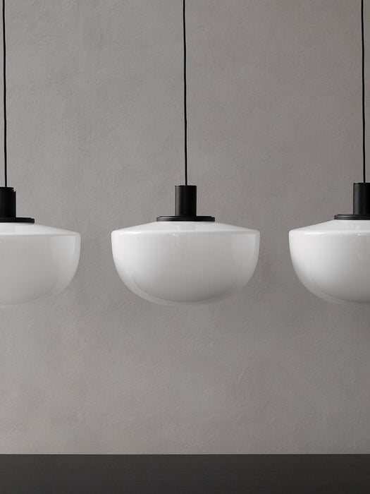 A close-up of three white opal glass Bank Pendant lights with black fittings, hanging in a row against a textured grey wall.