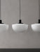 A close-up of three white opal glass Bank Pendant lights with black fittings, hanging in a row against a textured grey wall.