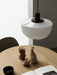 A close-up of the Bank Pendant with an opal glass shade and black fitting, hanging over a wooden table with clay sculptures.