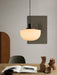 The Bank Pendant light with an opal glass shade glows over a wooden table with an open book and clay sculptures.