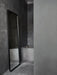 The tall, black-framed Norm Floor Mirror by Norm Architects leaning against a dark grey, stone-tiled wall in a bathroom.