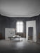 The tall, black-framed Norm Floor Mirror stands in a minimalist room with dark walls, a daybed, and a hanging copper lamp.