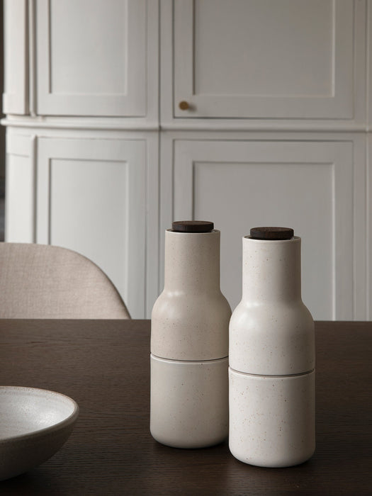 Two off-white speckled ceramic Bottle Grinders with wooden tops sit on the dark wood Adrogyne Dining Table.