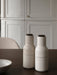 Two off-white speckled ceramic Bottle Grinders with wooden tops sit on the dark wood Adrogyne Dining Table.