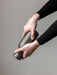 Close-up of two hands in black sleeves twisting the dark grey, matte Bottle Grinder from Audo Copenhagen on grey background.