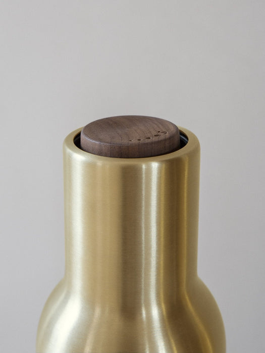 A close-up shot of the top of a Bottle Grinder, showing its brushed brass body and dark walnut lid on a grey background.