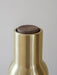 A close-up shot of the top of a Bottle Grinder, showing its brushed brass body and dark walnut lid on a grey background.