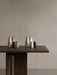 A collection of Audo Bottle Grinders in muted, earthy tones on the corner of a dark wood Androgyne Dining Table.