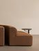 The black, round-topped Branch Side Table placed next to the arm of a brown Eave Seamline sofa against a beige wall.