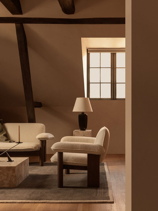A cosy, dimly lit attic room featuring a cream bouclé Brasilia Lounge Chair, with a matching sofa and Torso Table Lamp.