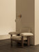The Brasilia Lounge Chair in beige sheepskin sits below the brass TR Bulb Suspended Wall Lamp against a neutral-toned wall.