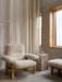 The Brasilia Lounge Chair and Ottoman in sheepskin sit by a Plint Cubic marble table in a serene room with large windows.