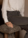 A person in a patterned shirt and jeans sits in the Brasilia Lounge Chair, hand resting on the plush, dark sheepskin armrest.
