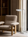 A close-up of the Brasilia Lounge Chair in beige upholstery and an oak frame, placed on a Houkime Rug next to a floor lamp.
