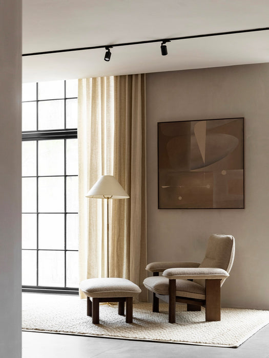 The Brasilia Lounge Chair and Brasilia Ottoman in beige fabric, placed on a Houkime Rug in a bright, modern living room.