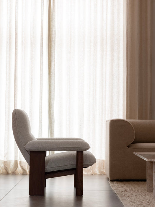 Side view of the Brasilia Lounge Chair with its dark wood frame and light fabric, set in a living room beside an Eave Sofa.
