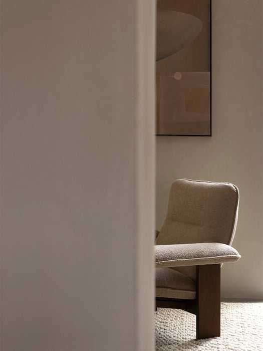 Partial view of the Brasilia Lounge Chair in beige textile with dark wood frame, sitting on a textured Houkime Rug.
