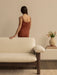 Back view of a woman resting her hand on a cream Brasilia Sofa. To the right, a vase of tulips sits on a stack of books.