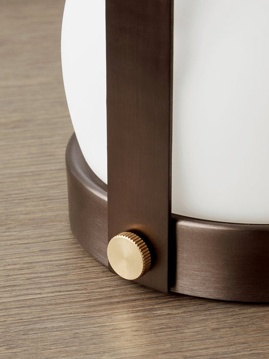 Close-up of the bronzed brass Carrie Table Lamp, detailing the textured brass knob and opal glass shade on a wooden surface.